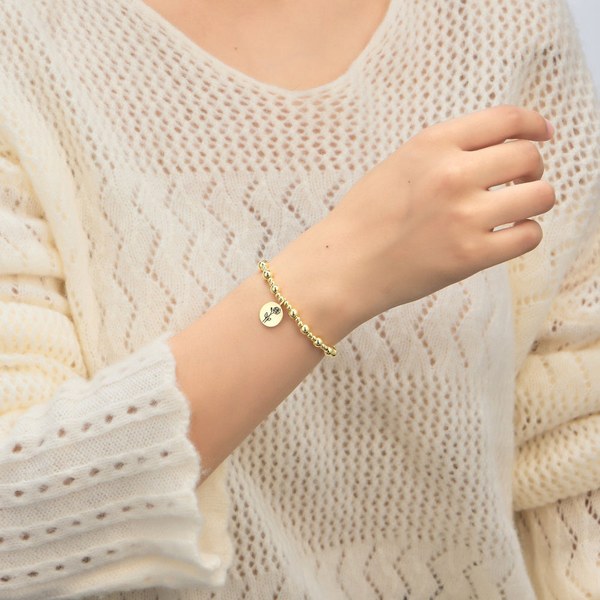 Woman in a cream knit jumper wearing a Philip Jones gold June birth flower bracelet