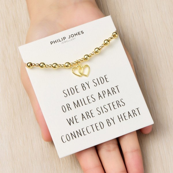 Hand holding a Philip Jones sister heart link bracelet on its quote card