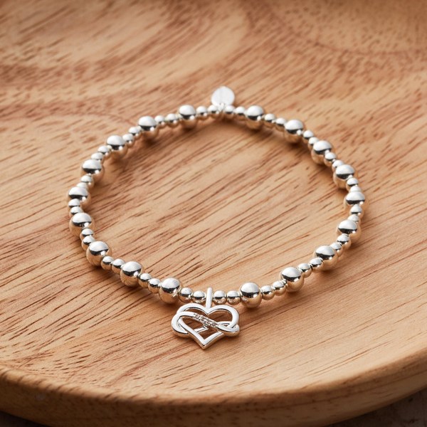 Philip Jones silver plated infinity heart beaded stretch bracelet on a wooden surface