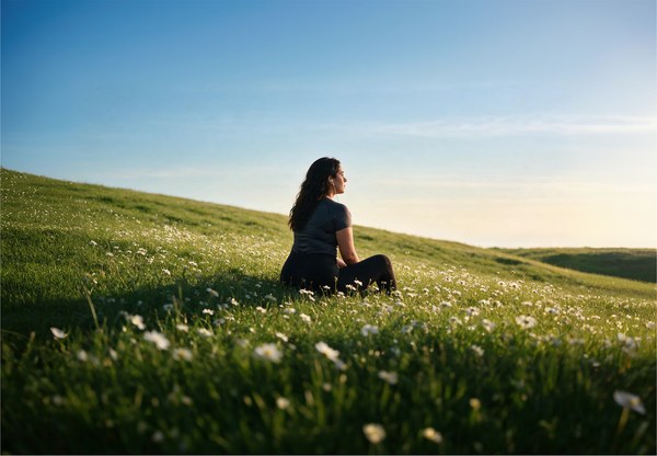 Person sitting on a grassy hillside at sunrise surrounded by wildflowers