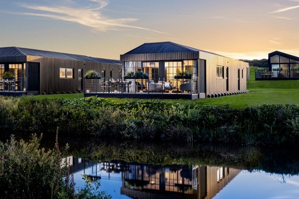 A modern lodge with a decked terrace beside a lake at dusk