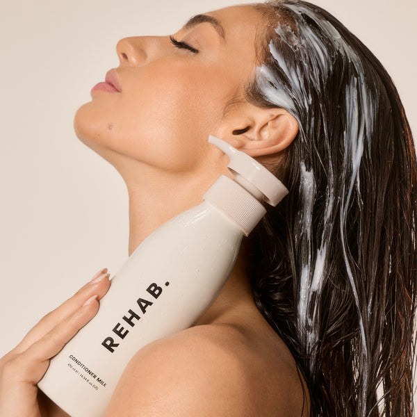 Woman holding a bottle of REHAB Conditioner Milk with conditioner through her hair