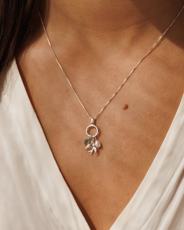 How to Build a Charm Necklace: Chains, Holders and Charms Explained Woman wearing a fine gold chain with a Gldn collector pendant holding small charms
