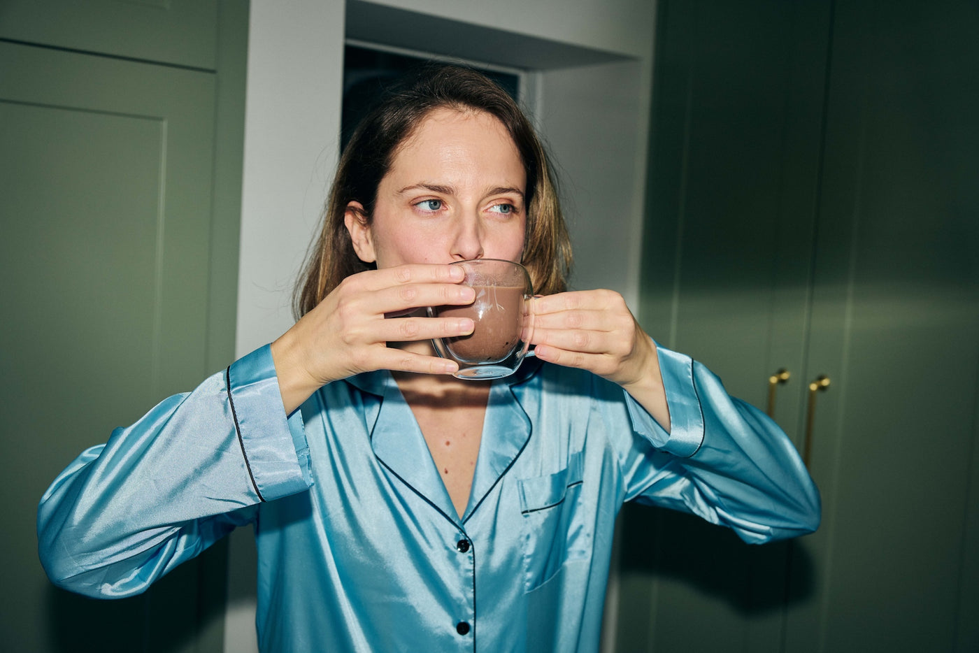 Woman in silk pyjamas sipping a warm drink from a glass cup