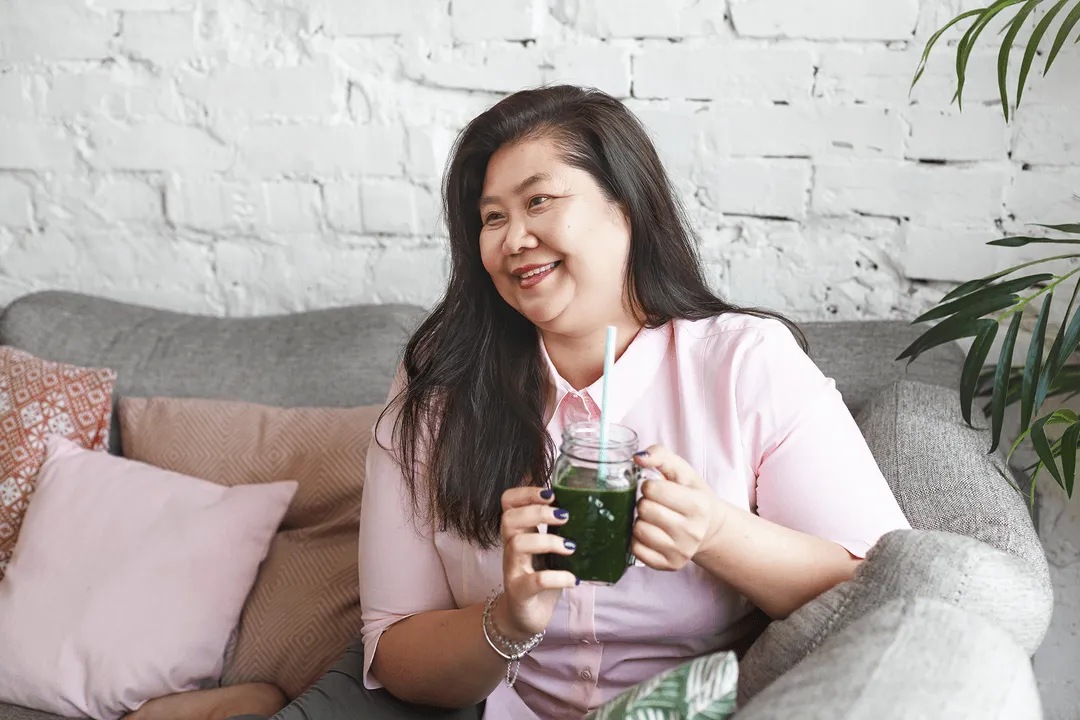 Smiling woman relaxing on a sofa with a green smoothie
