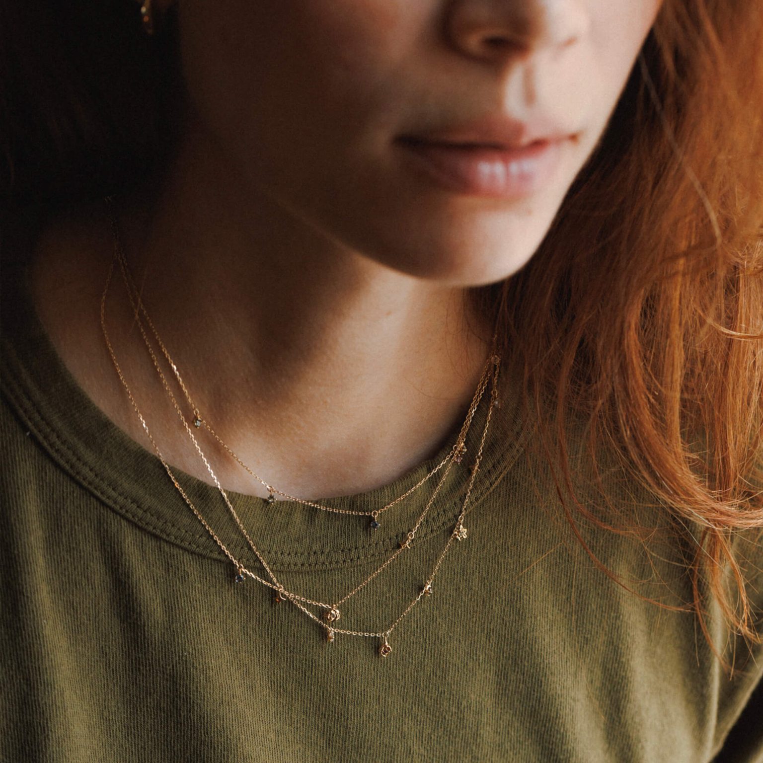 Woman wearing several layered gold necklaces with a green t-shirt