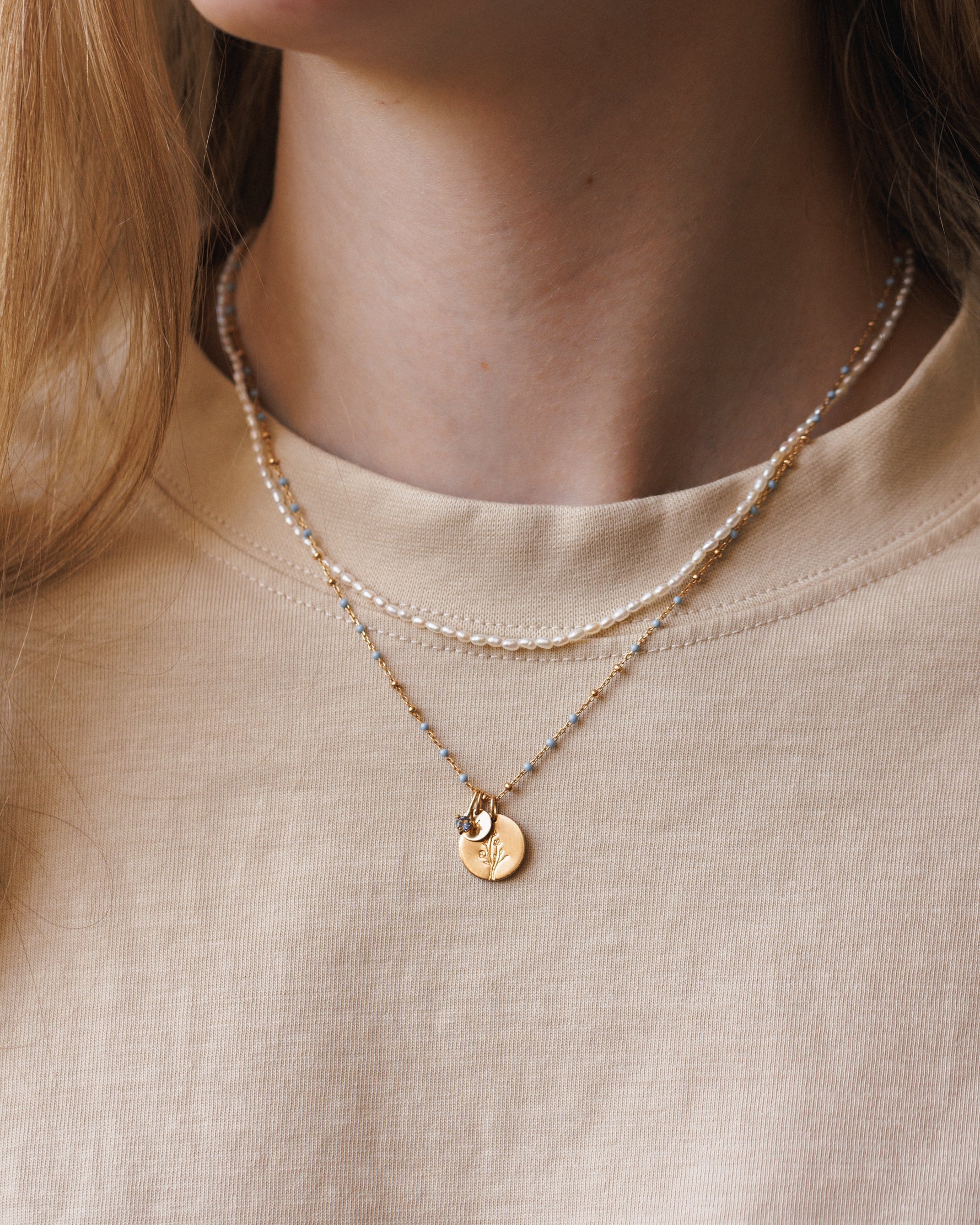 Layered pearl strand and gold coin pendant necklaces worn with a cream t-shirt