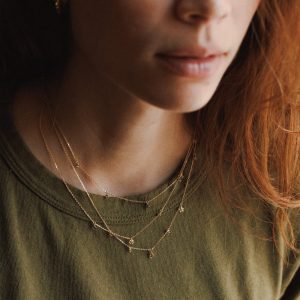 Woman wearing several layered gold necklaces with a green t-shirt