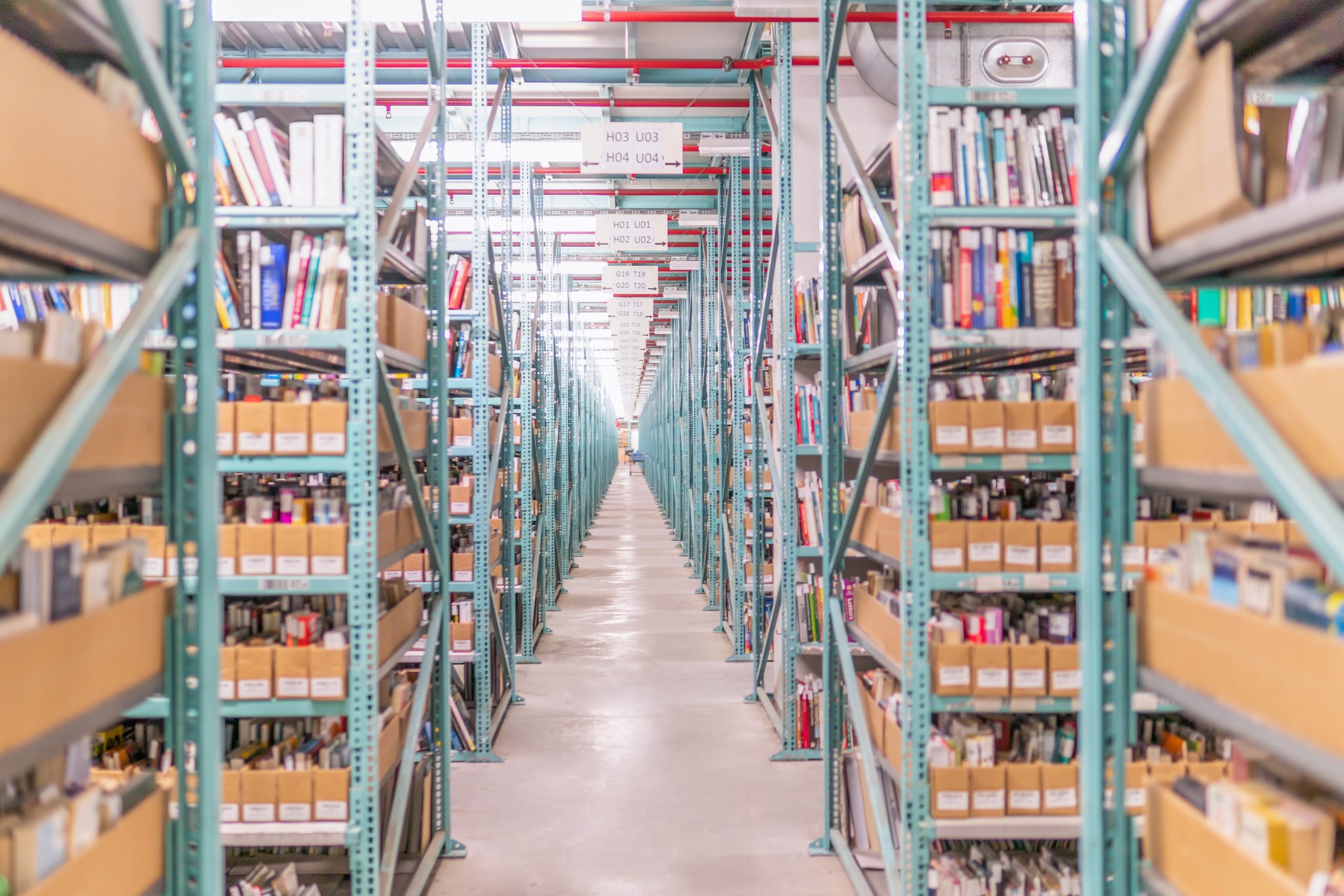 A long warehouse aisle lined with shelves of second-hand books and media