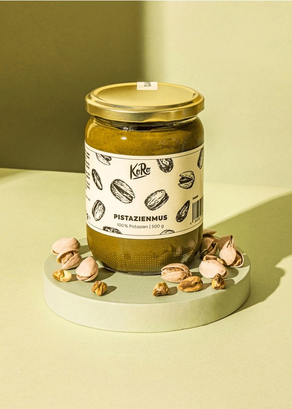 KoRo pistachio butter jar surrounded by pistachios on a pastel background
