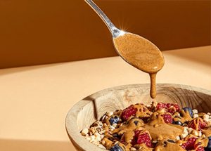 Spoon drizzling nut butter over a bowl of muesli with berries, from the KoRo nut butter category