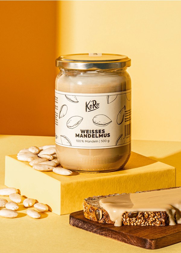 KoRo white almond butter jar next to almonds and a slice of bread