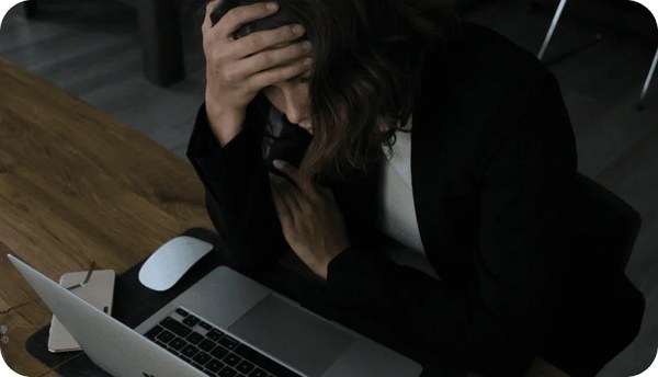 Person with head in hand in front of a laptop, stressed about bills
