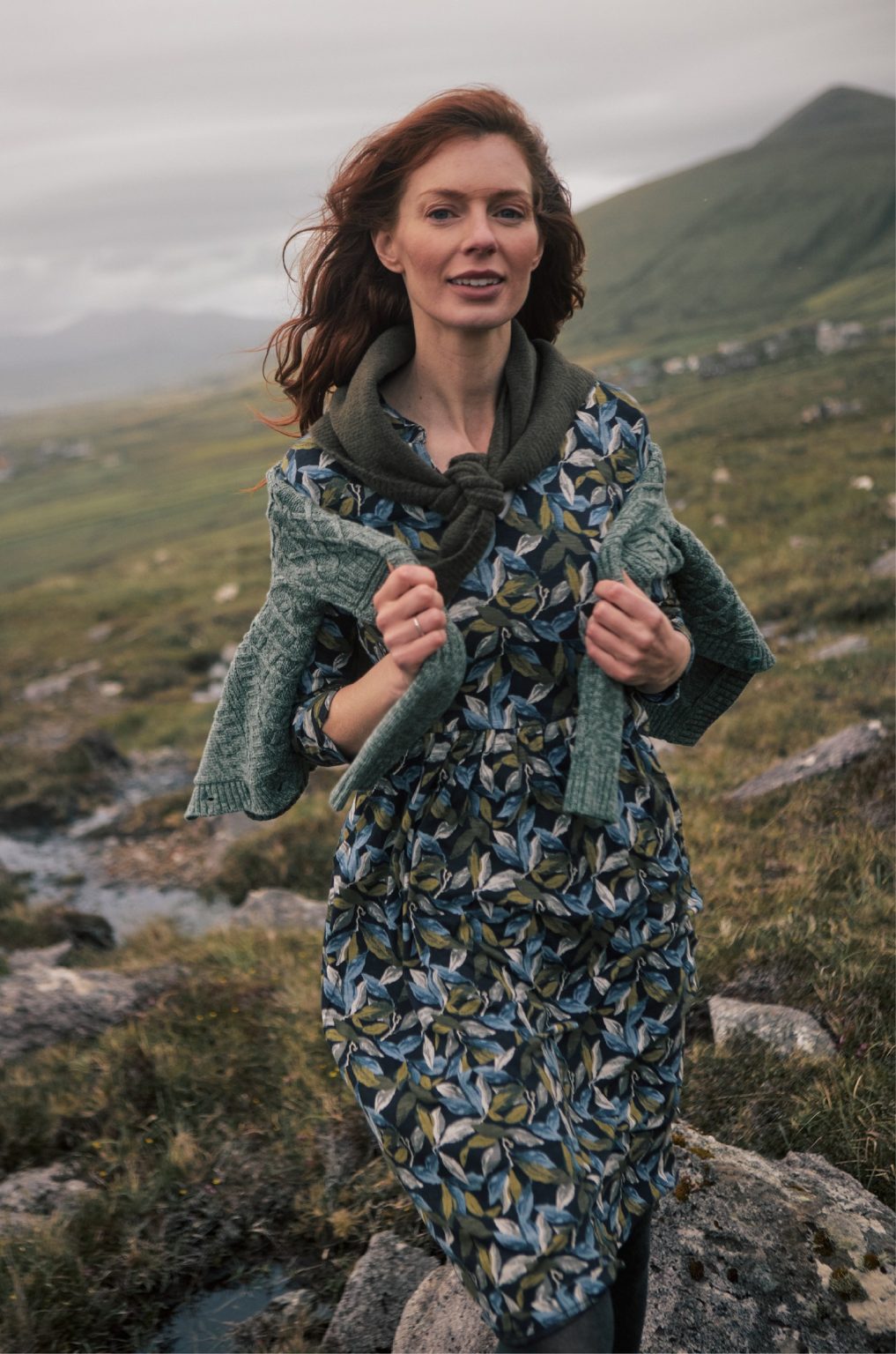 Woman in a floral dress and green cardigan on a rugged coastal hillside